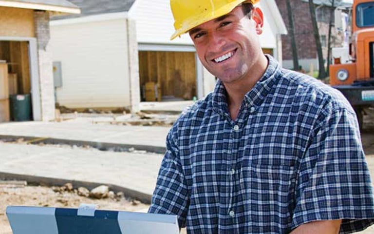 Contractor in hard hat smiling outside home construction.