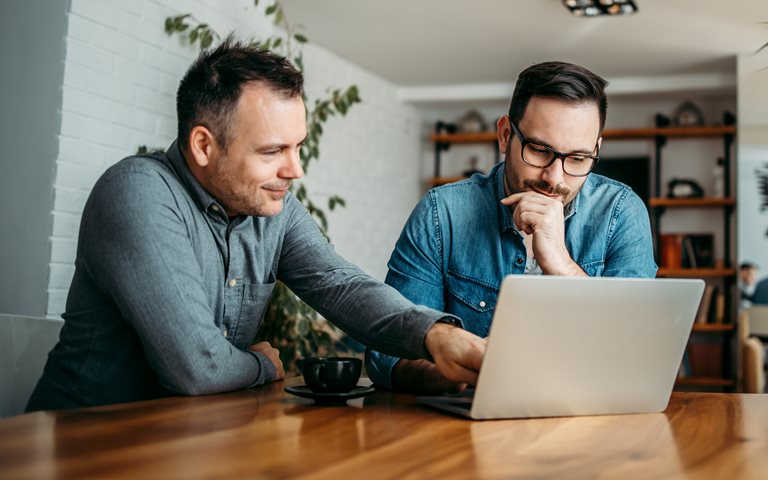 Two people sitting at a desk table looking at a laptop.