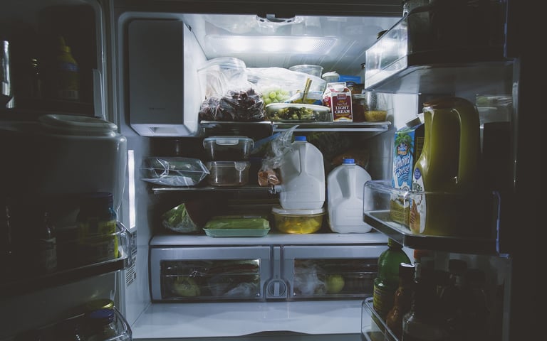 Dark kitchen with open refrigerator full of groceries with light on.